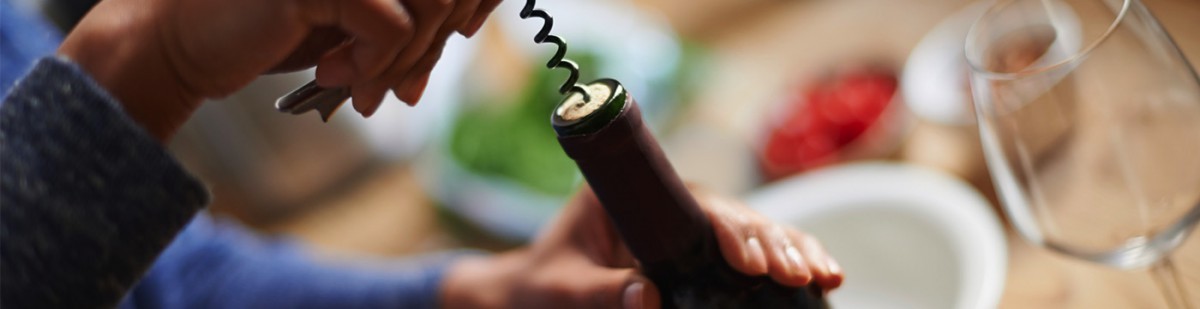 Person opening a bottle of red wine with a corkscrew at a dinner table