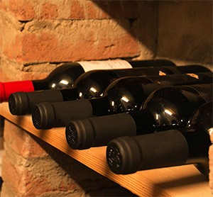 Bottles of wine lying on their sides in a wooden cellar rack against a stone wall