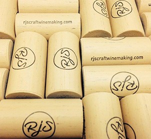 A pile of natural corks branded with the RJS logo and rjscraftwinemaking.com