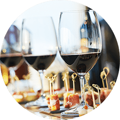 Glasses of red wine lined up on a table beside trays of canapes on cocktail sticks