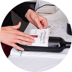 Hands smoothing an En Primeur label onto a bottle of red wine lying on a table