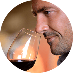 A man tilting a glass of red wine to his nose to smell it