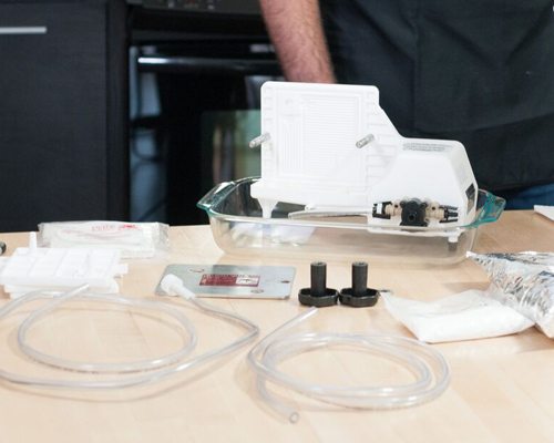 Plate filter parts laid out on a counter: the pump unit in a glass tray, filter pads, clear tubing and fittings