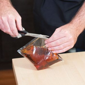 Hands snipping open a pouch of amber sweetening blend with scissors on a wooden counter