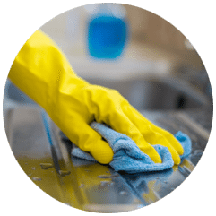 A yellow-gloved hand wiping down a stainless steel counter with a blue microfibre cloth