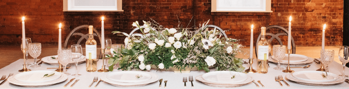 Wedding reception table with a white floral centrepiece, candles and bottles of white wine
