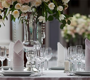 Banquet table set with white flowers, folded napkins and rows of empty wine glasses