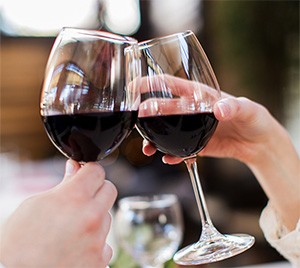 Two people touching glasses of red wine together across a table