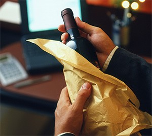 Hands unwrapping a bottle of wine from gold tissue paper at an office desk